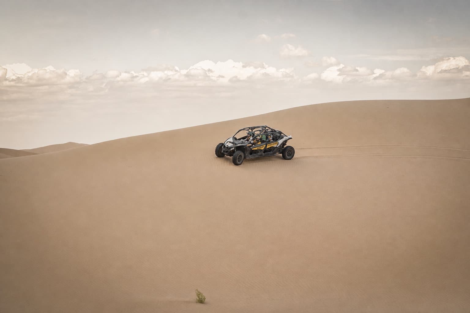 A small open field vehicle carrying a group across a vast dune slope