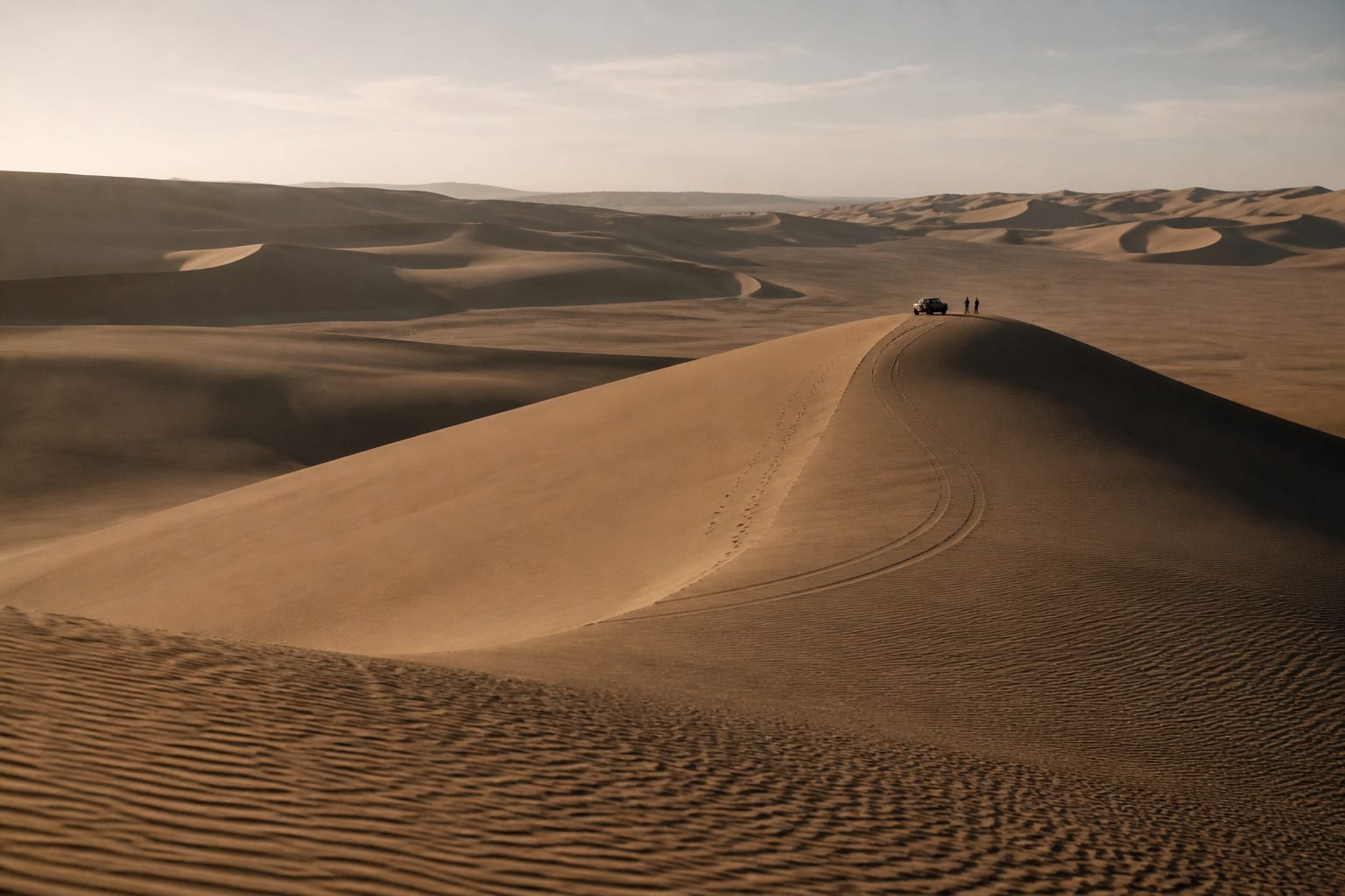 A small anonymous group and vehicle paused on a vast dune ridge