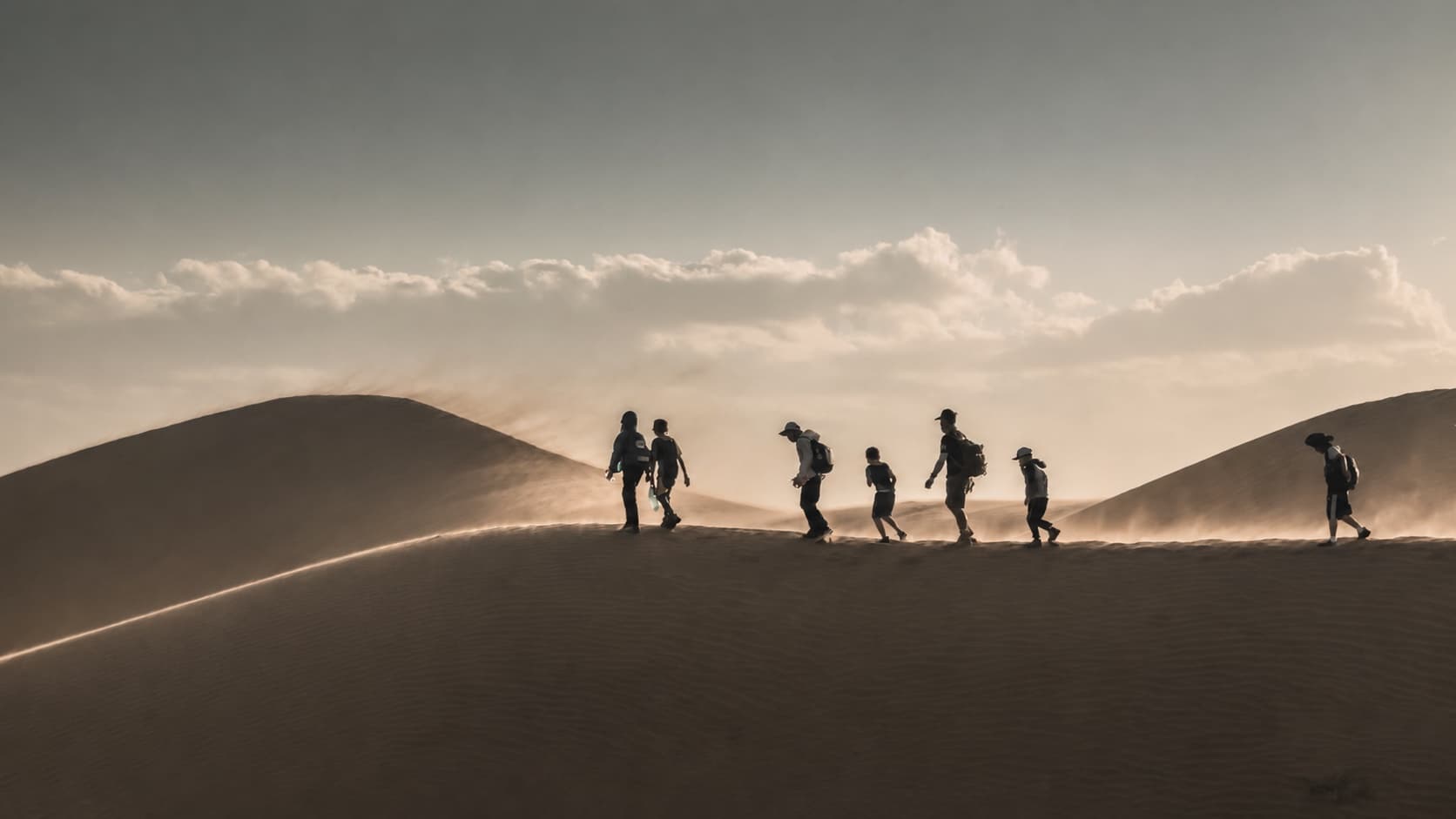 A small group walking along a wind-swept dune ridge in late desert light